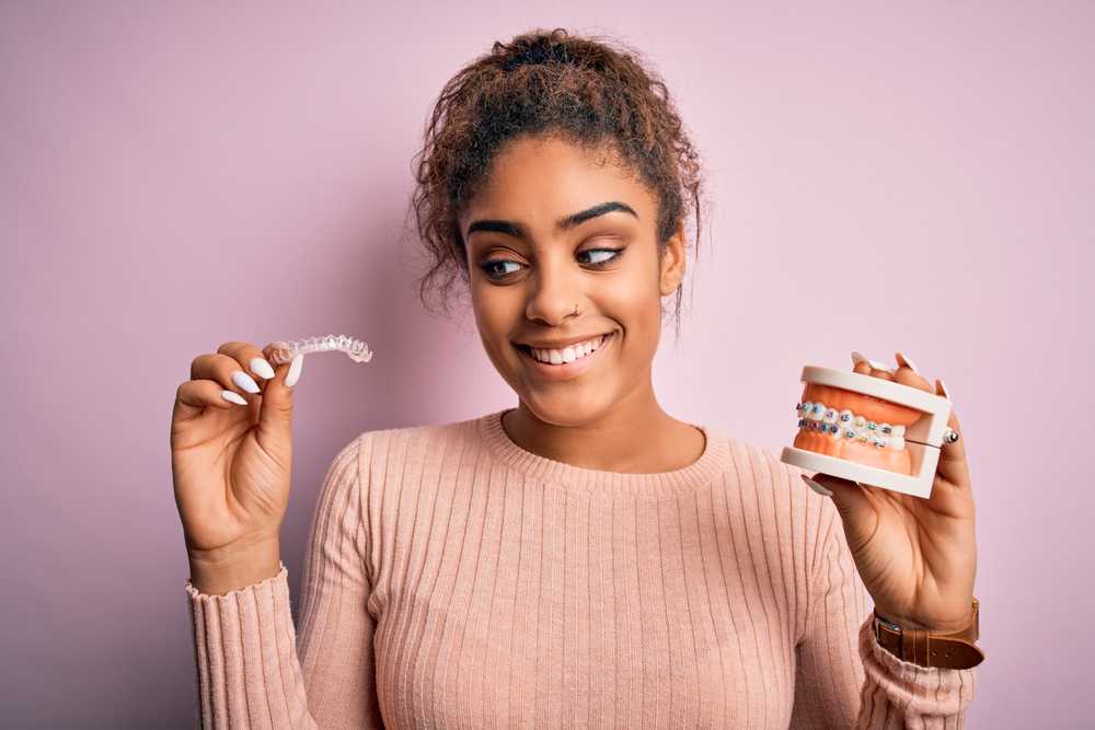 Woman holding model of teeth with braces in one hand and invisalign retainer in the other